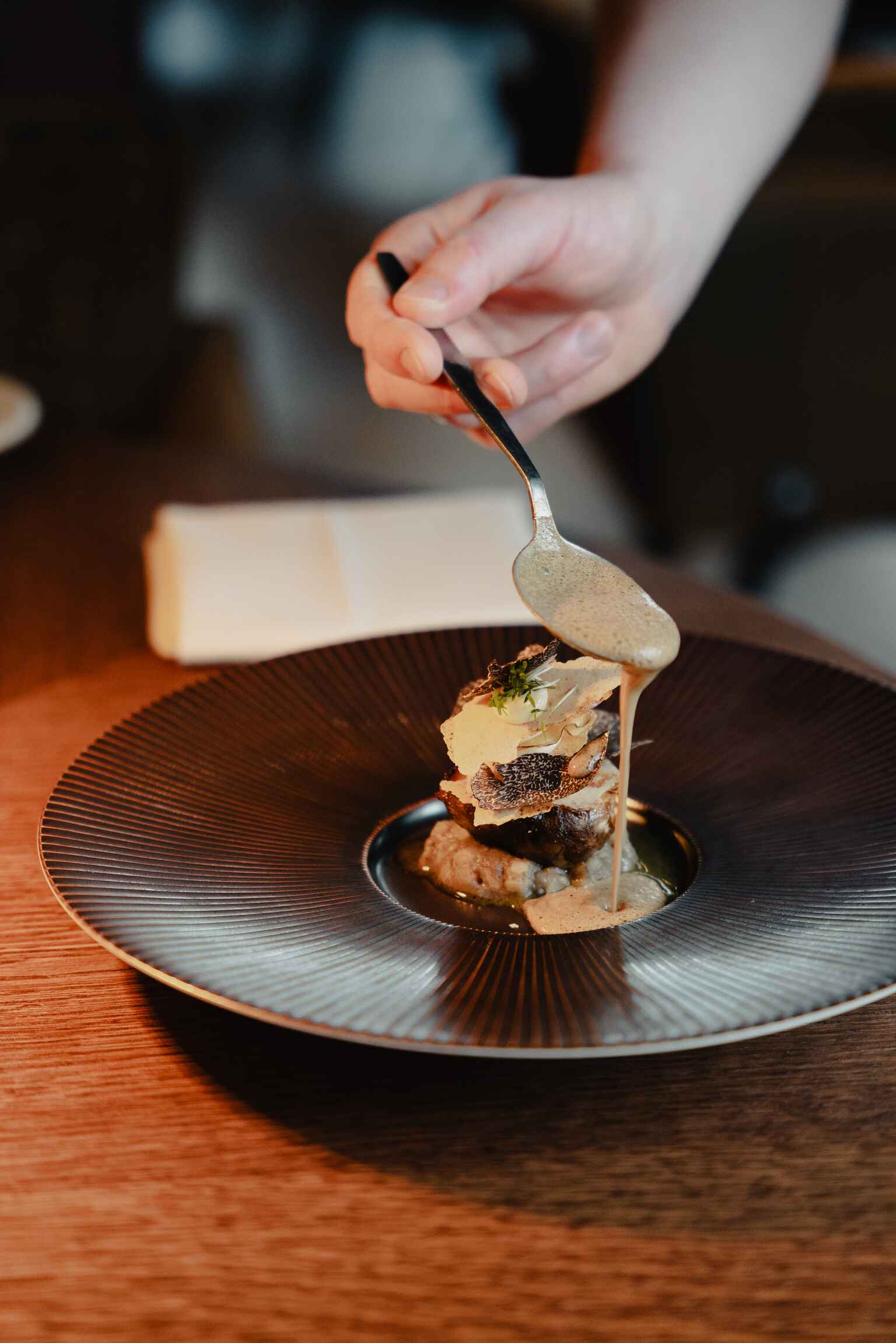 Hand schenkt romige saus over een verfijnd gerecht op een donker bord