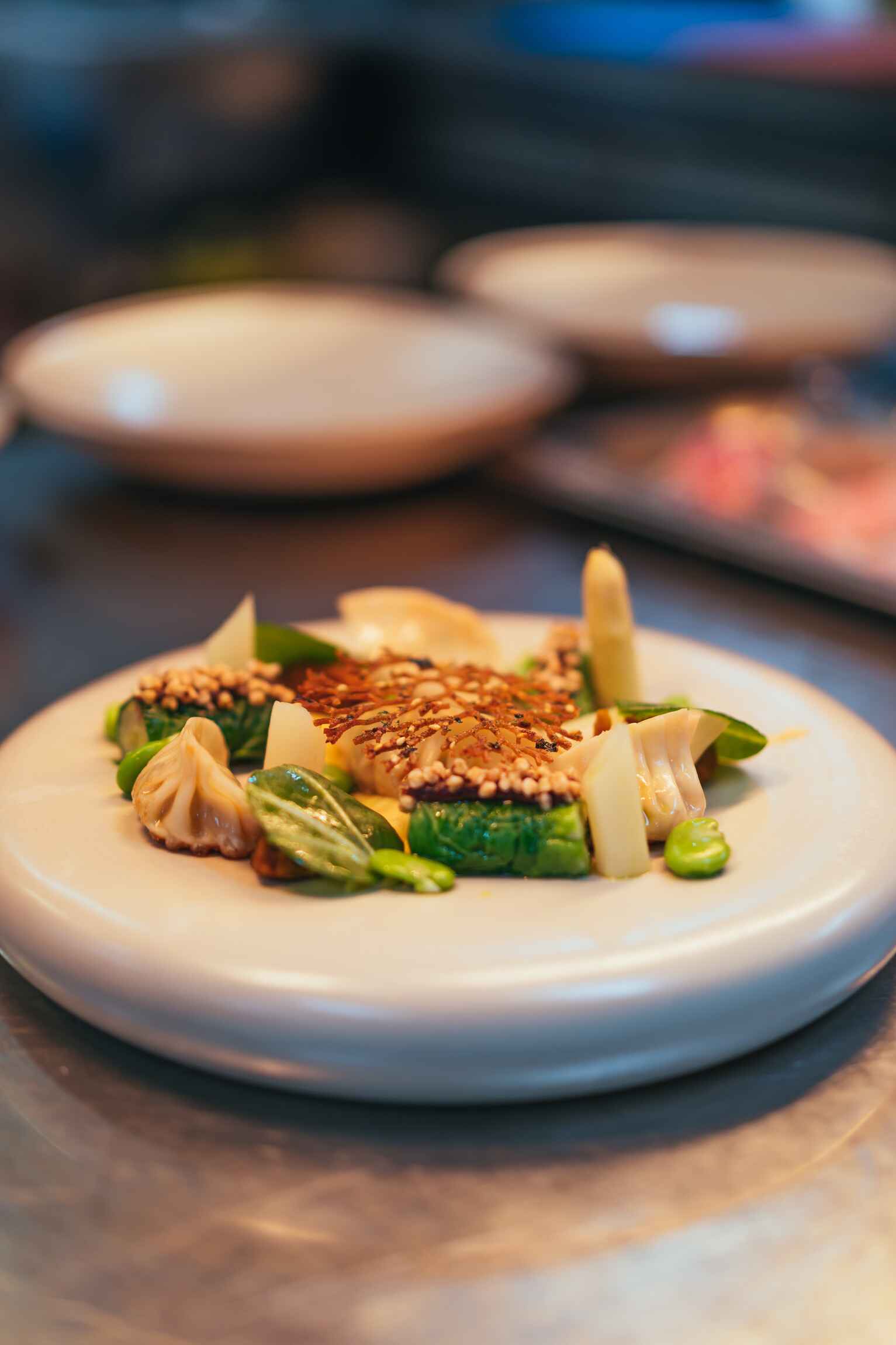 Verfijnd gerecht met sesam, witte asperge, tuinbonen en dumplings op een crèmekleurig bord